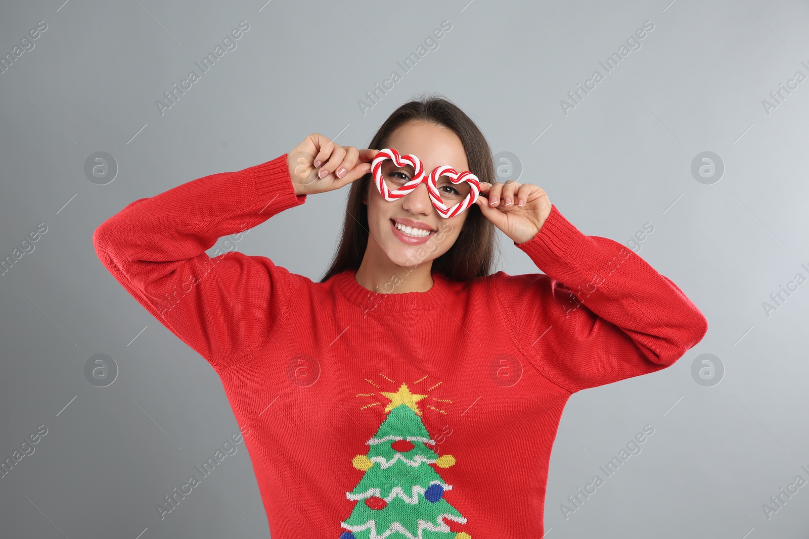 Young woman in Christmas sweater and party glasses on grey background Photo of Young woman in Christmas sweater and party glasses on grey background