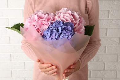 Photo of Woman with bouquet of beautiful hortensia flowers near white brick wall, closeup