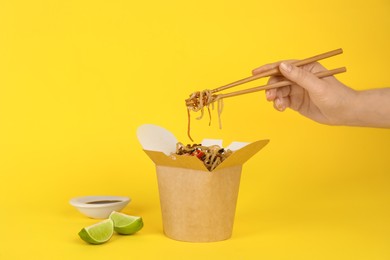 Woman eating seafood wok noodles with chopsticks from box on yellow background, closeup Photo of Woman eating seafood wok noodles with chopsticks from box on yellow background, closeup