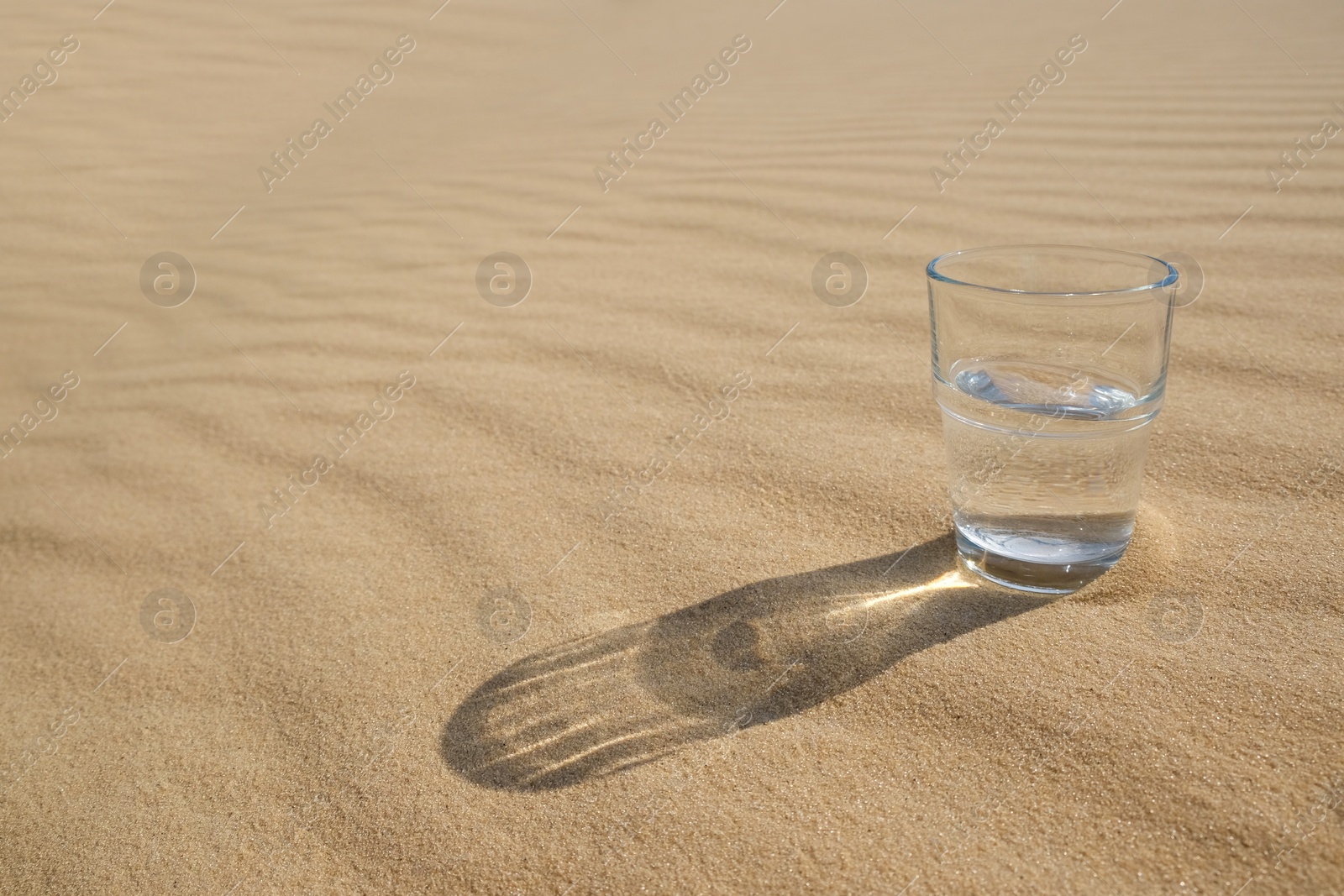 Glass of water on sand in desert. Space for text Photo of Glass of water on sand in desert. Space for text