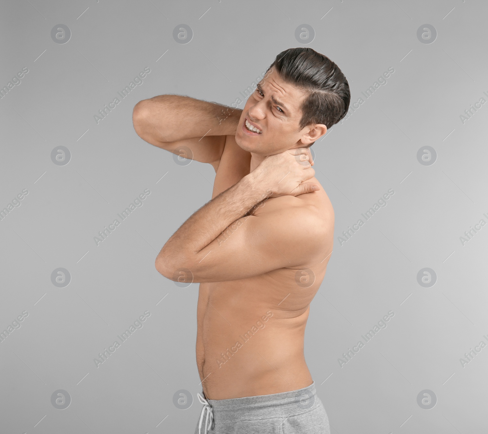 Young man suffering from neck pain on grey background Photo of Young man suffering from neck pain on grey background
