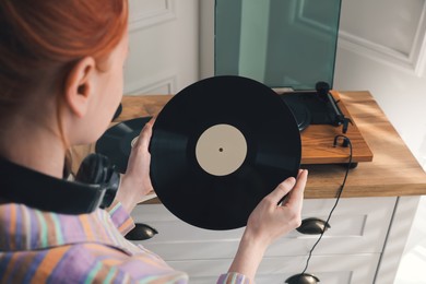 Young woman with vinyl disc near turntable at home Photo of Young woman with vinyl disc near turntable at home