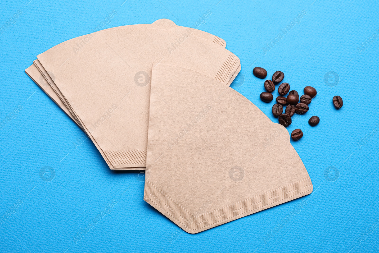 Photo of Paper coffee filters and beans on light blue background, above view