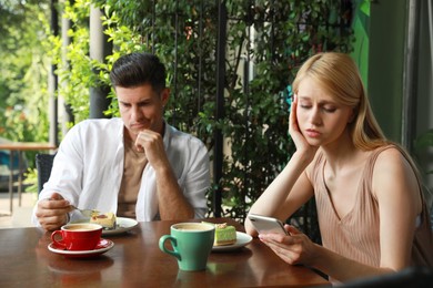 Young woman with smartphone ignoring her boyfriend in outdoor cafe. Boring date Photo of Young woman with smartphone ignoring her boyfriend in outdoor cafe. Boring date