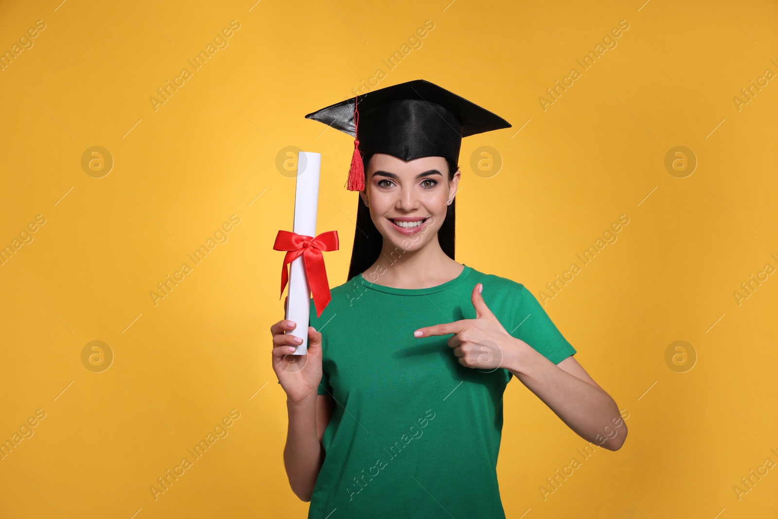 Happy student with graduation hat and diploma on yellow background Photo of Happy student with graduation hat and diploma on yellow background