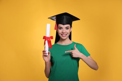 Happy student with graduation hat and diploma on yellow background Photo of Happy student with graduation hat and diploma on yellow background