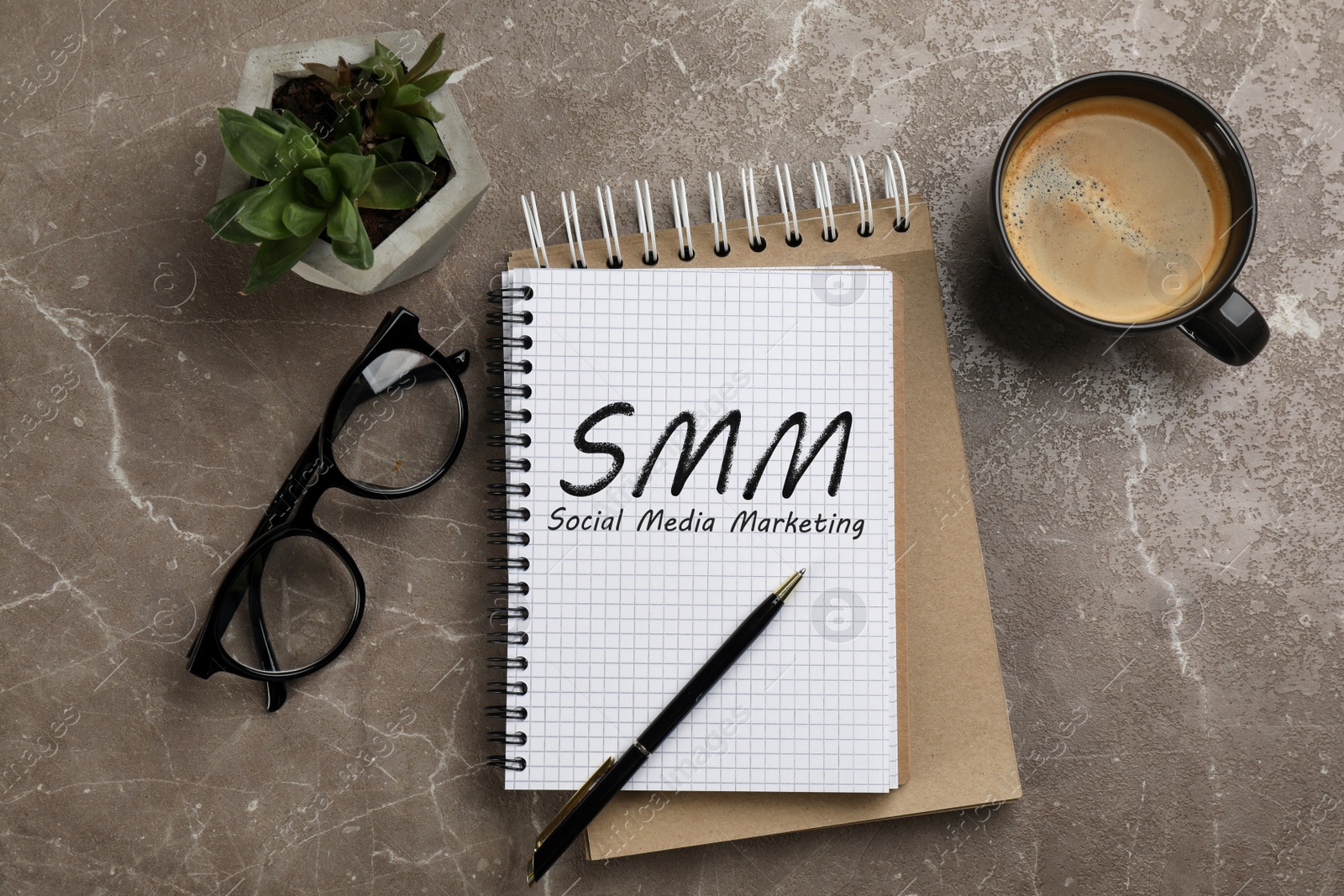 Notebook with text SMM (Social media marketing), cup of aromatic coffee, glasses and plant on brown marble table, flat lay Image of Notebook with text SMM (Social media marketing), cup of aromatic coffee, glasses and plant on brown marble table, flat lay