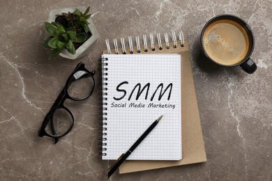 Notebook with text SMM (Social media marketing), cup of aromatic coffee, glasses and plant on brown marble table, flat lay Image of Notebook with text SMM (Social media marketing), cup of aromatic coffee, glasses and plant on brown marble table, flat lay