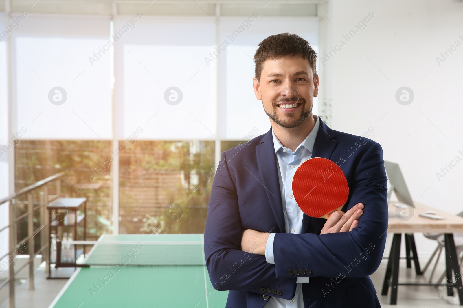 Businessman with tennis racket near ping pong table in office. Space for text Photo of Businessman with tennis racket near ping pong table in office. Space for text