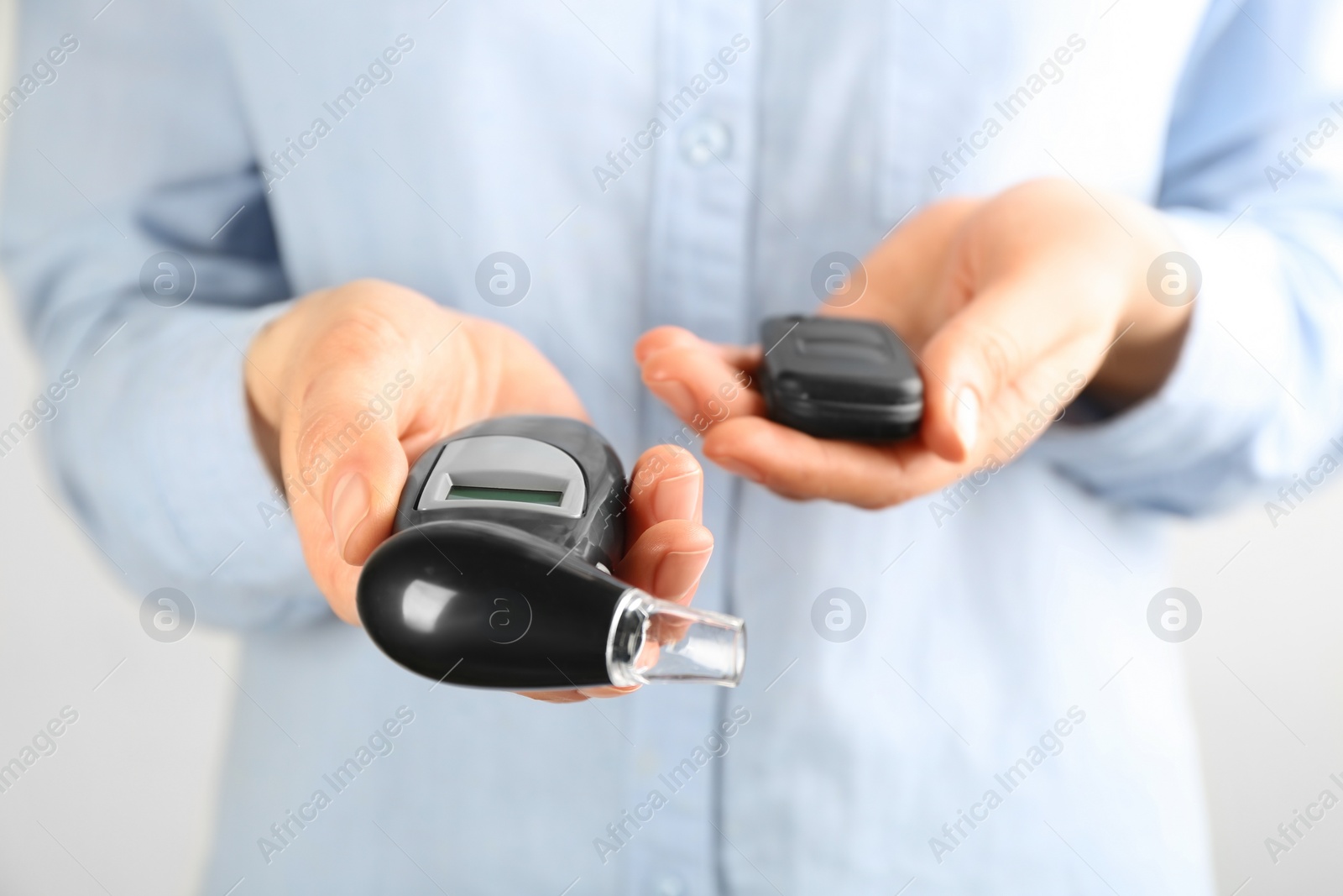 Woman holding modern breathalyzer and car key on light background, closeup Photo of Woman holding modern breathalyzer and car key on light background, closeup