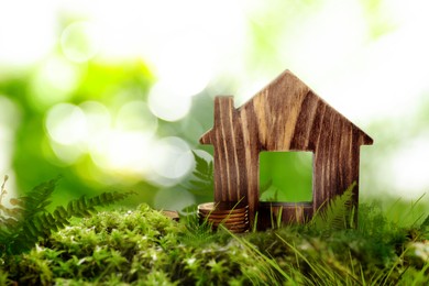 Eco friendly home. House model and coins on green grass outdoors, space for text Image of Eco friendly home. House model and coins on green grass outdoors, space for text