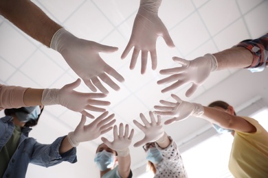 People in white medical gloves joining hands on light background, low angle view Photo of People in white medical gloves joining hands on light background, low angle view