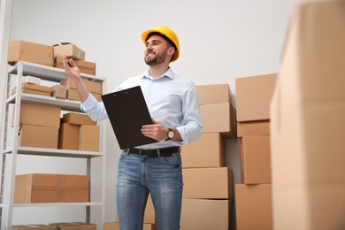 Young man with clipboard near cardboard boxes at warehouse Photo of Young man with clipboard near cardboard boxes at warehouse