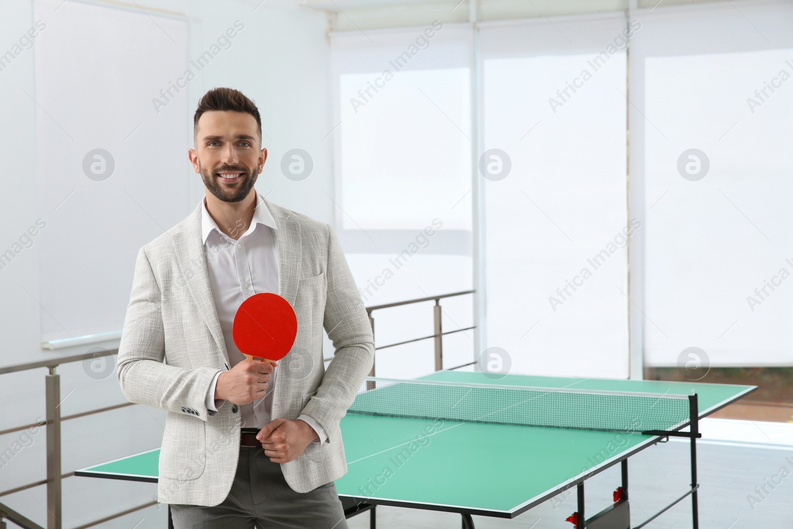 Businessman with tennis racket near ping pong table in office. Space for text Photo of Businessman with tennis racket near ping pong table in office. Space for text