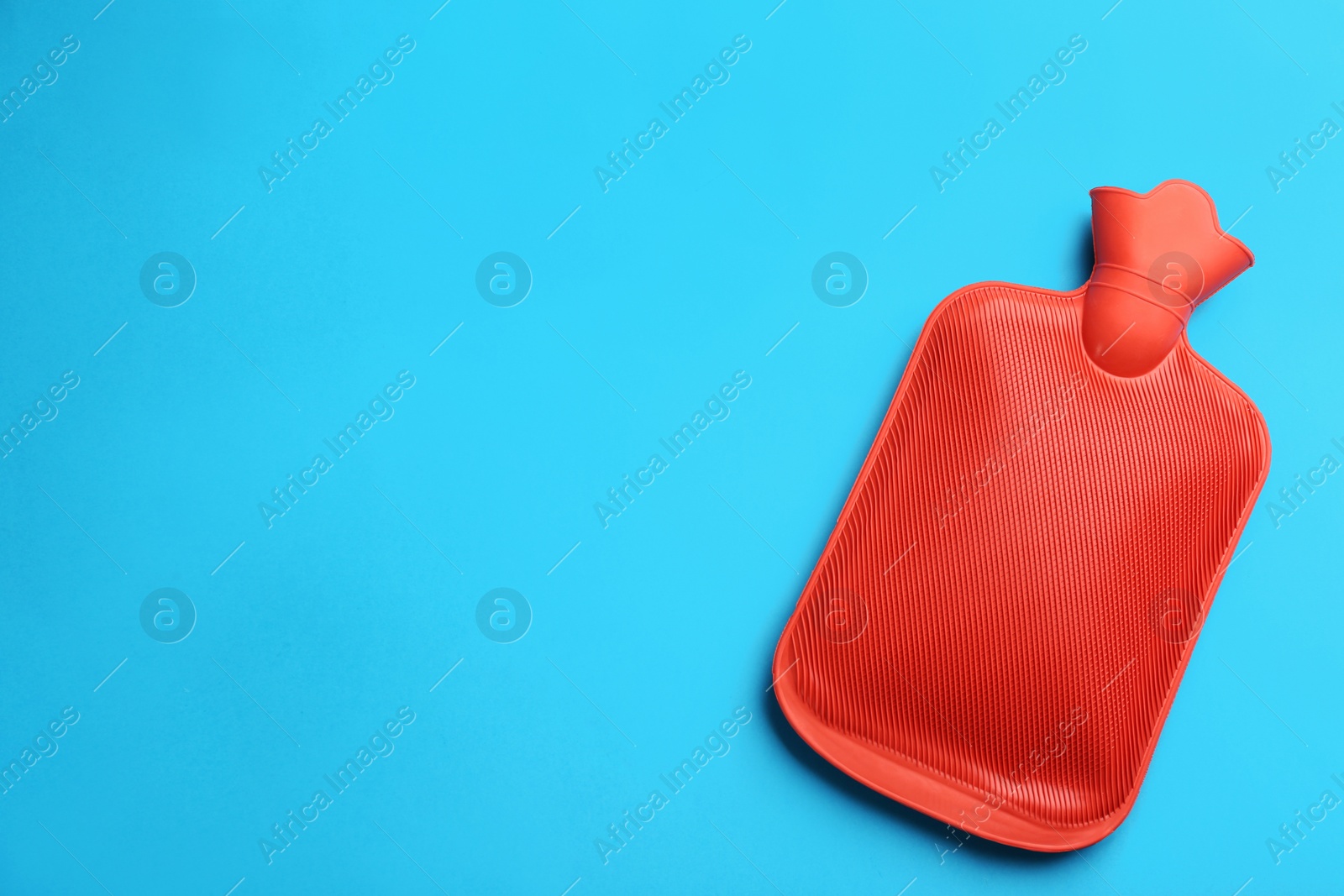 Photo of Red rubber hot water bottle on light blue background, top view. Space for text