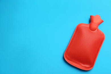 Photo of Red rubber hot water bottle on light blue background, top view. Space for text