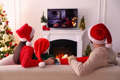 Family watching festive movie on TV in room decorated for Christmas, back view Image of Family watching festive movie on TV in room decorated for Christmas, back view