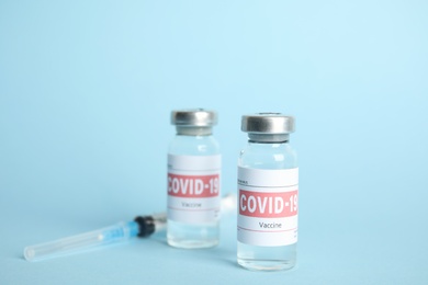 Vials with coronavirus vaccine and syringe on light blue background Photo of Vials with coronavirus vaccine and syringe on light blue background