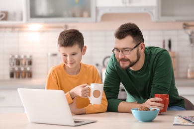Little boy and his dad using laptop in kitchen Photo of Little boy and his dad using laptop in kitchen