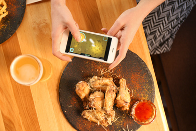 Woman playing game using smartphone at table with tasty BBQ wings, top view Photo of Woman playing game using smartphone at table with tasty BBQ wings, top view