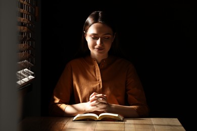 Religious young woman praying over Bible at wooden table indoors Photo of Religious young woman praying over Bible at wooden table indoors