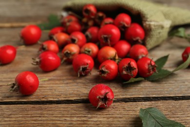Ripe rose hip berries with green leaves on wooden table, closeup Photo of Ripe rose hip berries with green leaves on wooden table, closeup