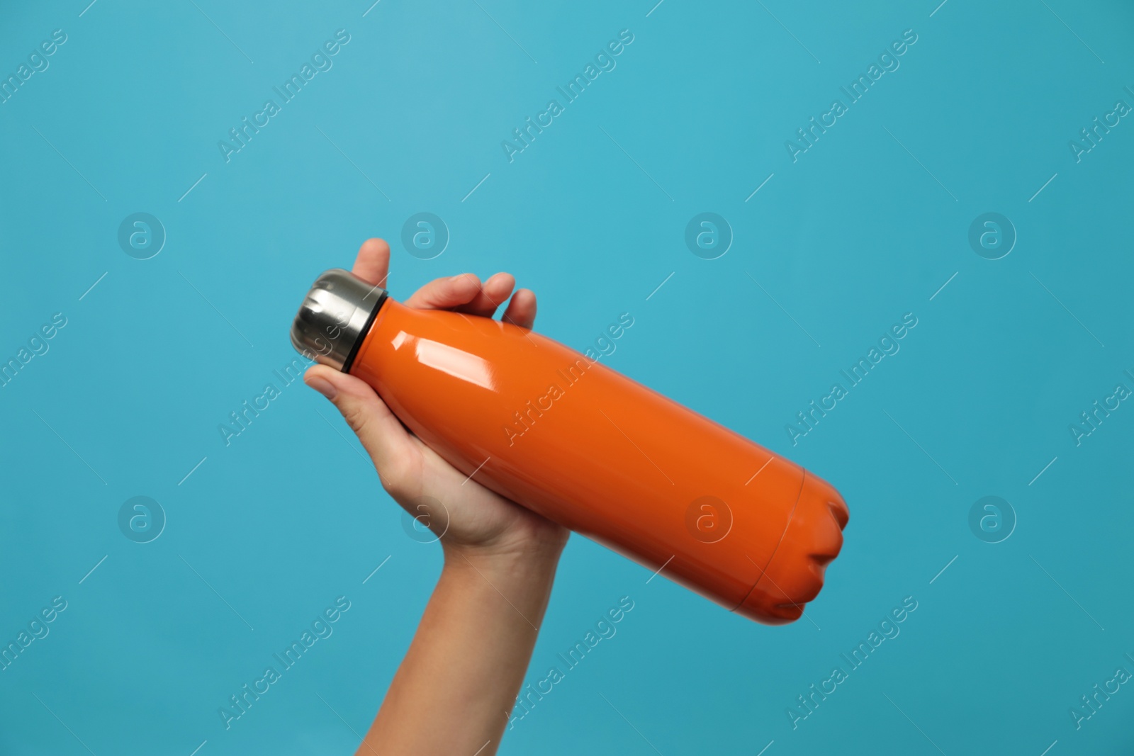 Photo of Woman holding modern orange thermos on light blue background, closeup