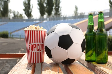Football ball with beer and popcorn on wooden bench in stadium Photo of Football ball with beer and popcorn on wooden bench in stadium