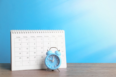 Calendar and alarm clock on wooden table against light blue background. Space for text Image of Calendar and alarm clock on wooden table against light blue background. Space for text