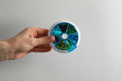 Woman holding plastic box with different pills on light grey background, closeup Photo of Woman holding plastic box with different pills on light grey background, closeup
