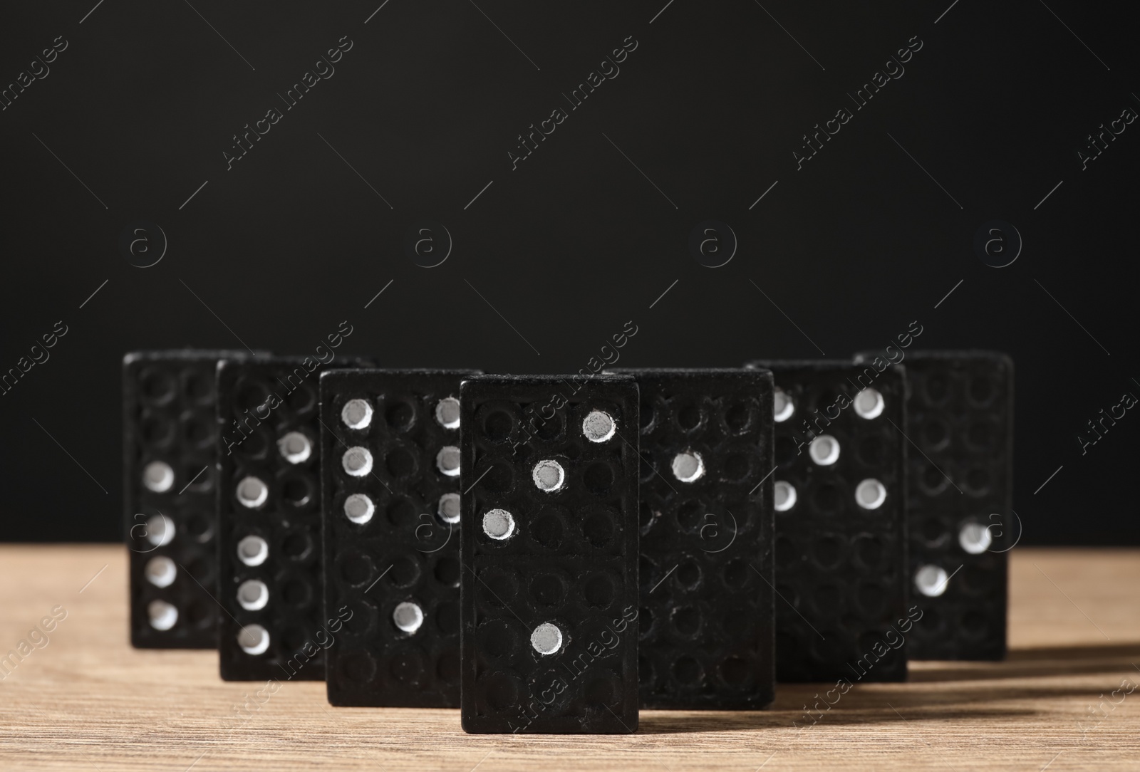 Photo of Domino tiles on wooden table against black background. Space for text