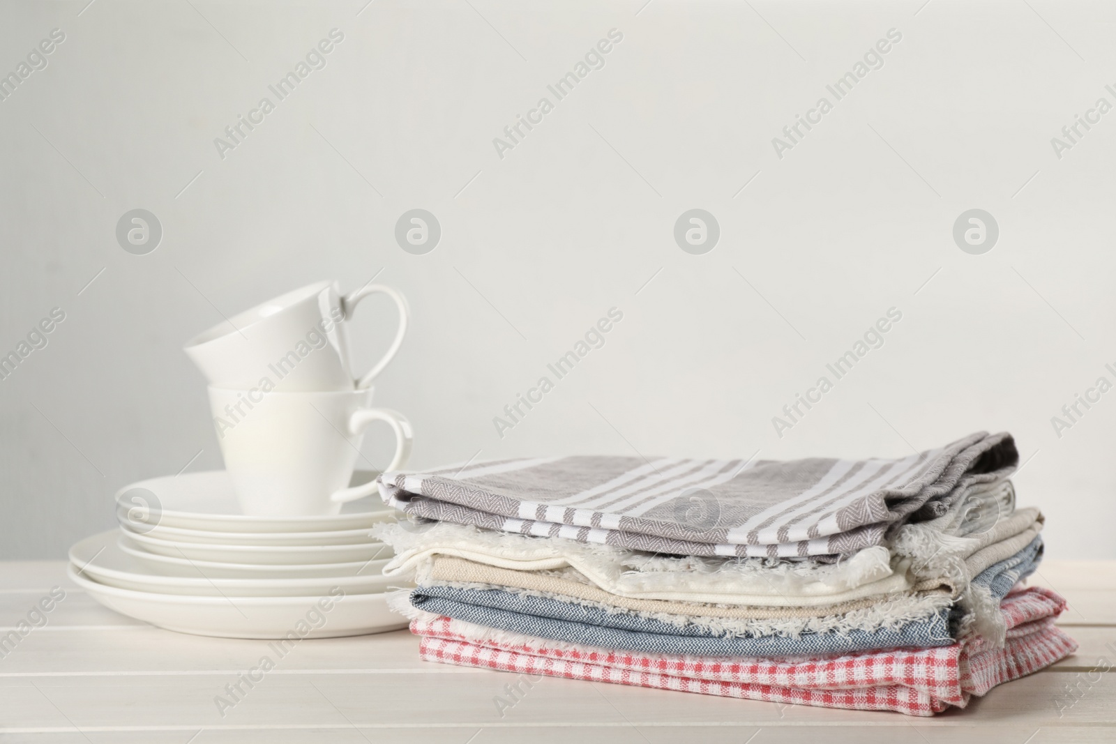 Stacked kitchen towels and dishware on white wooden table, space for text Photo of Stacked kitchen towels and dishware on white wooden table, space for text