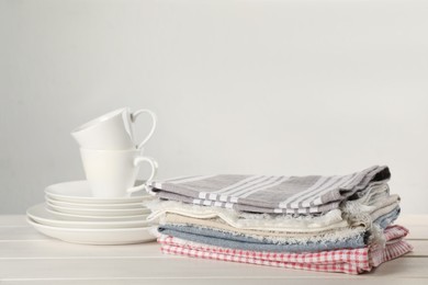 Stacked kitchen towels and dishware on white wooden table, space for text Photo of Stacked kitchen towels and dishware on white wooden table, space for text