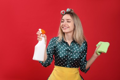 Young housewife with detergent and rag on red background Photo of Young housewife with detergent and rag on red background
