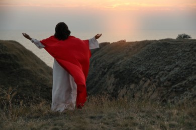 Jesus Christ raising hands on hills at sunset, back view. Space for text Photo of Jesus Christ raising hands on hills at sunset, back view. Space for text
