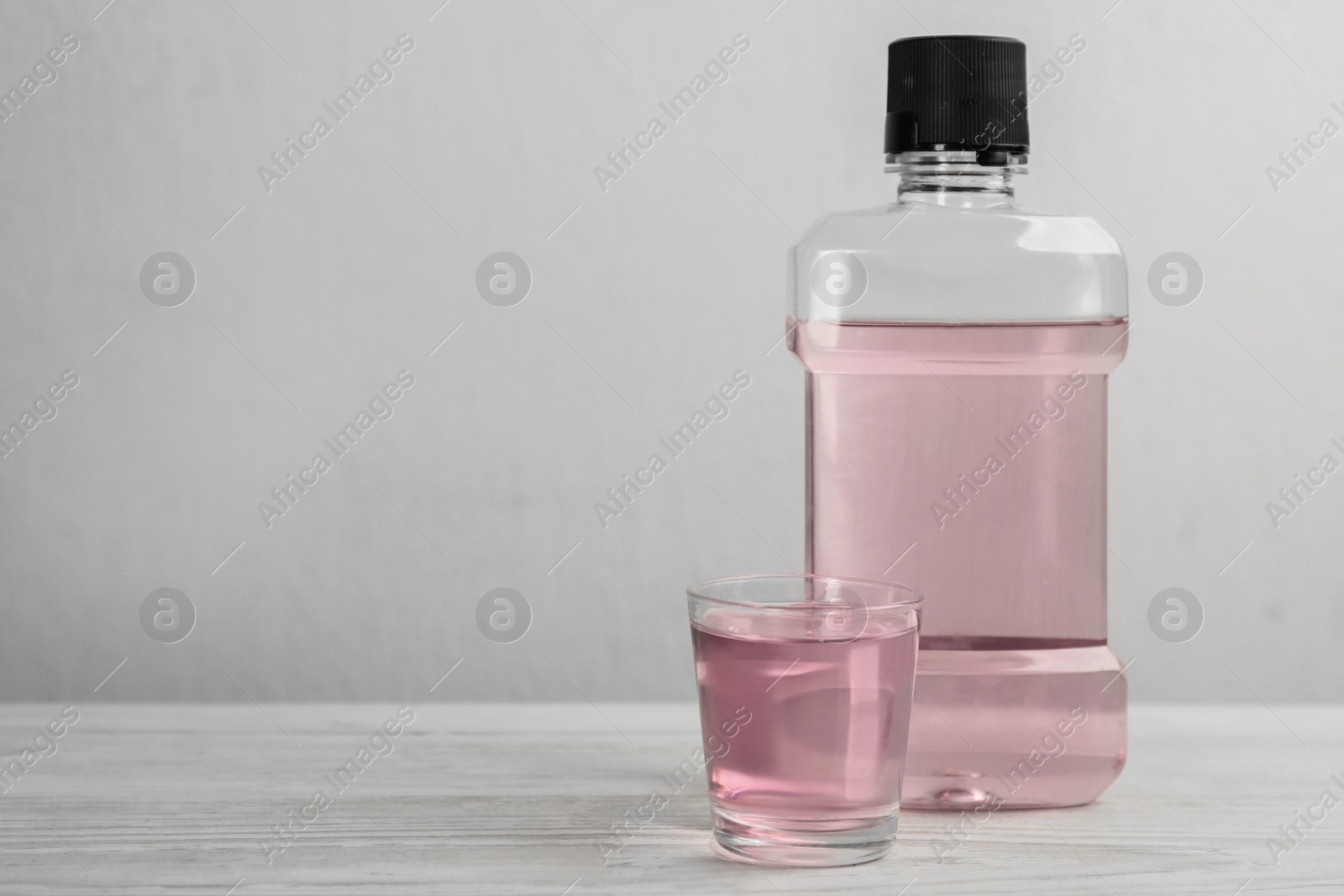 Bottle and glass with mouthwash on white wooden table, space for text Photo of Bottle and glass with mouthwash on white wooden table, space for text