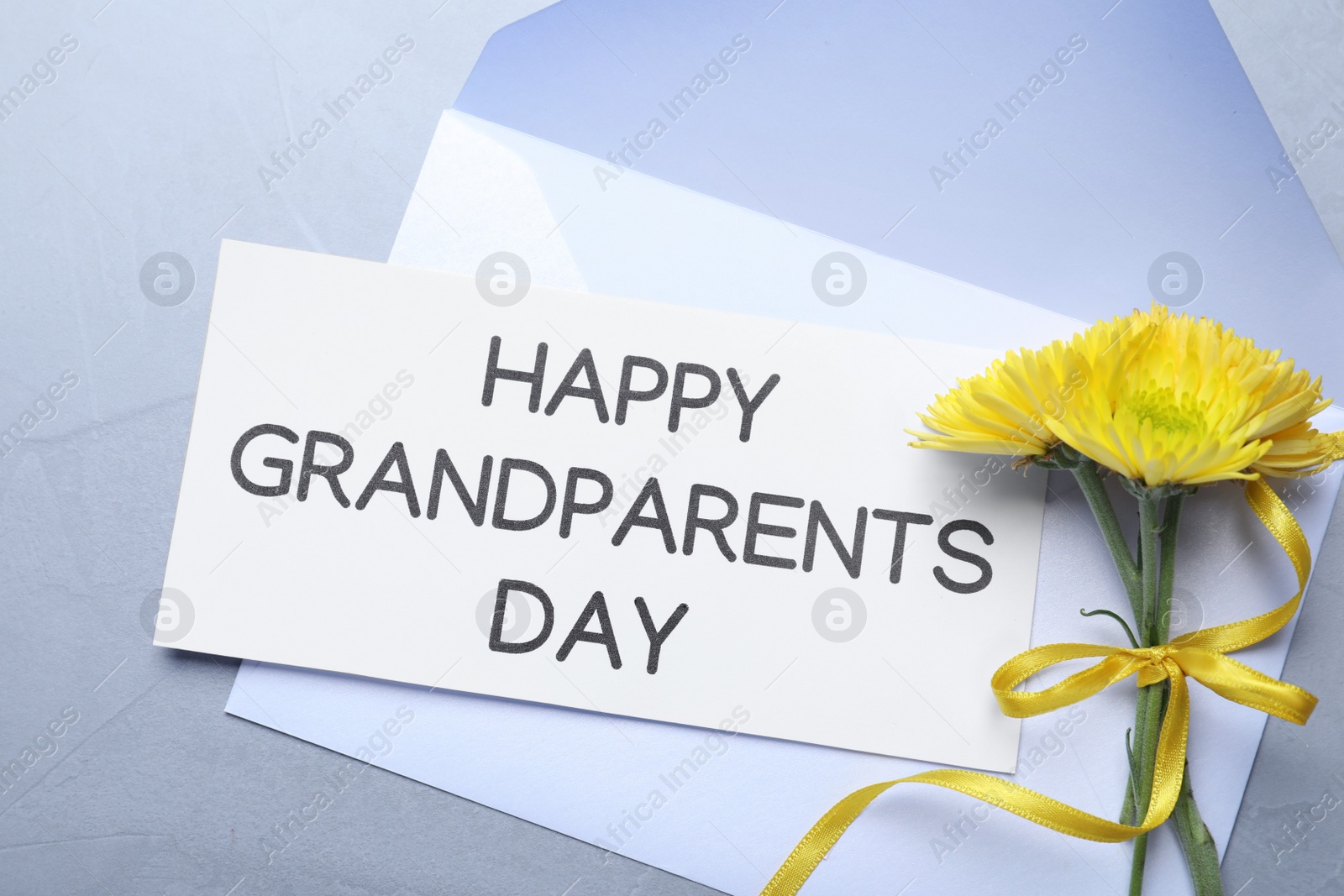 Card with phrase Happy Grandparents Day, envelope and beautiful flowers on grey background, flat lay Photo of Card with phrase Happy Grandparents Day, envelope and beautiful flowers on grey background, flat lay