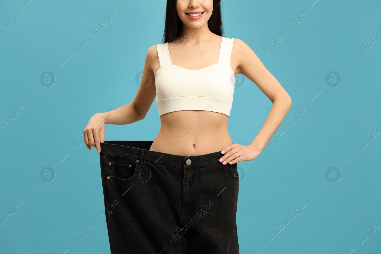 Happy young woman wearing big jeans after weight loss on turquoise background, closeup Photo of Happy young woman wearing big jeans after weight loss on turquoise background, closeup