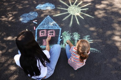 Little child and her mother drawing with colorful chalks on asphalt, above view Photo of Little child and her mother drawing with colorful chalks on asphalt, above view