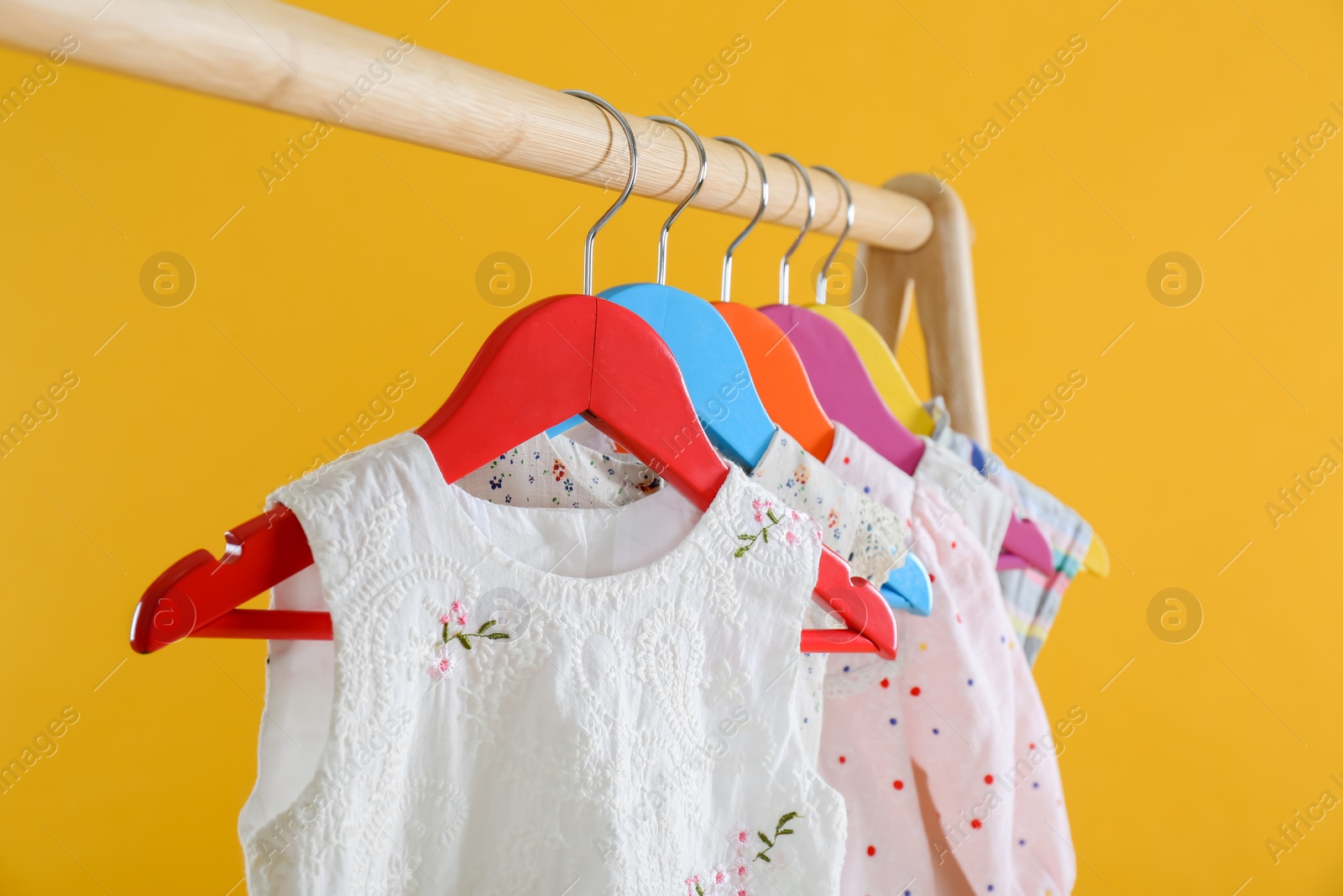 Rack with stylish children clothes on yellow background, closeup Photo of Rack with stylish children clothes on yellow background, closeup