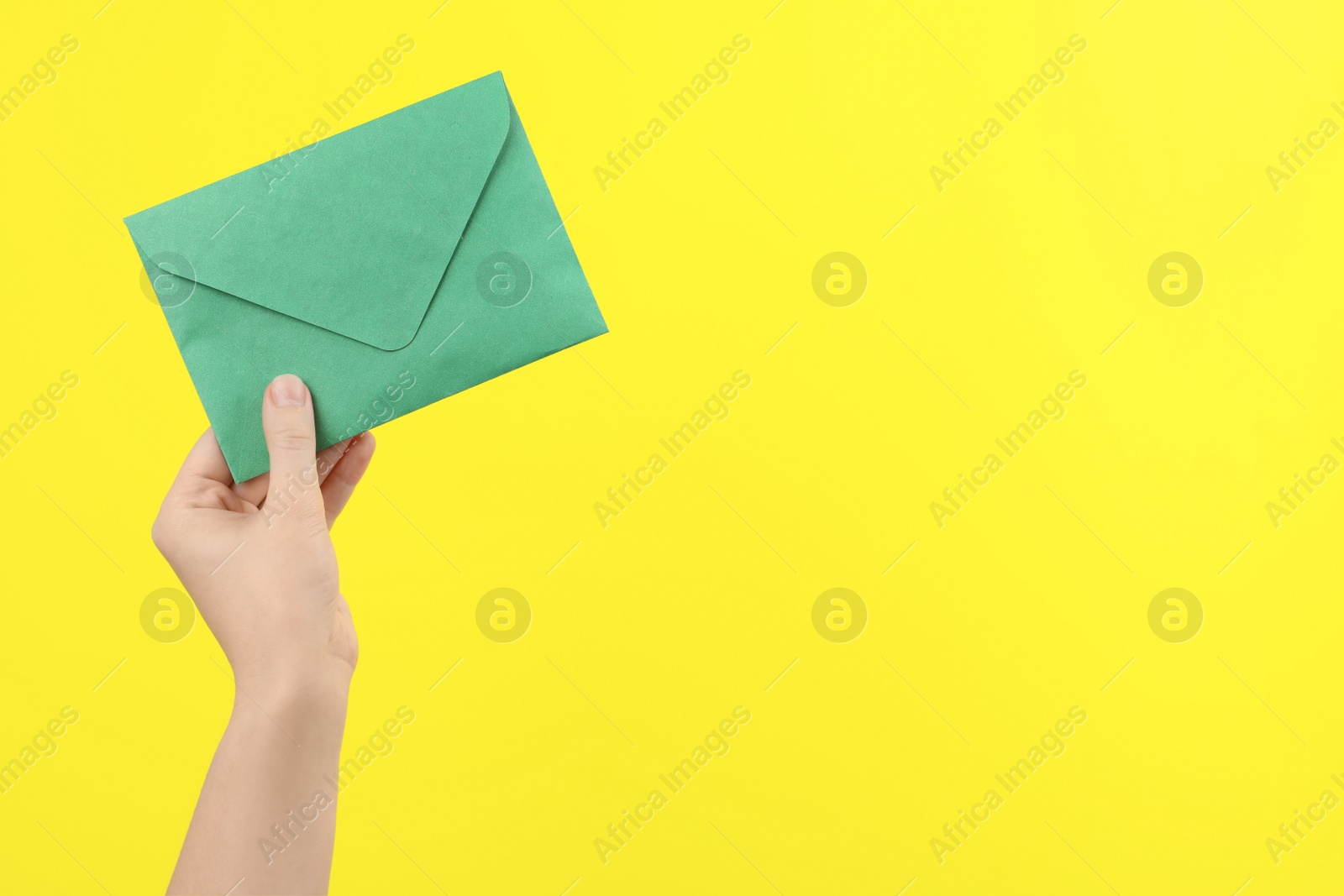 Woman holding green paper envelope on yellow background, closeup. Space for text Photo of Woman holding green paper envelope on yellow background, closeup. Space for text