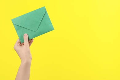 Woman holding green paper envelope on yellow background, closeup. Space for text Photo of Woman holding green paper envelope on yellow background, closeup. Space for text