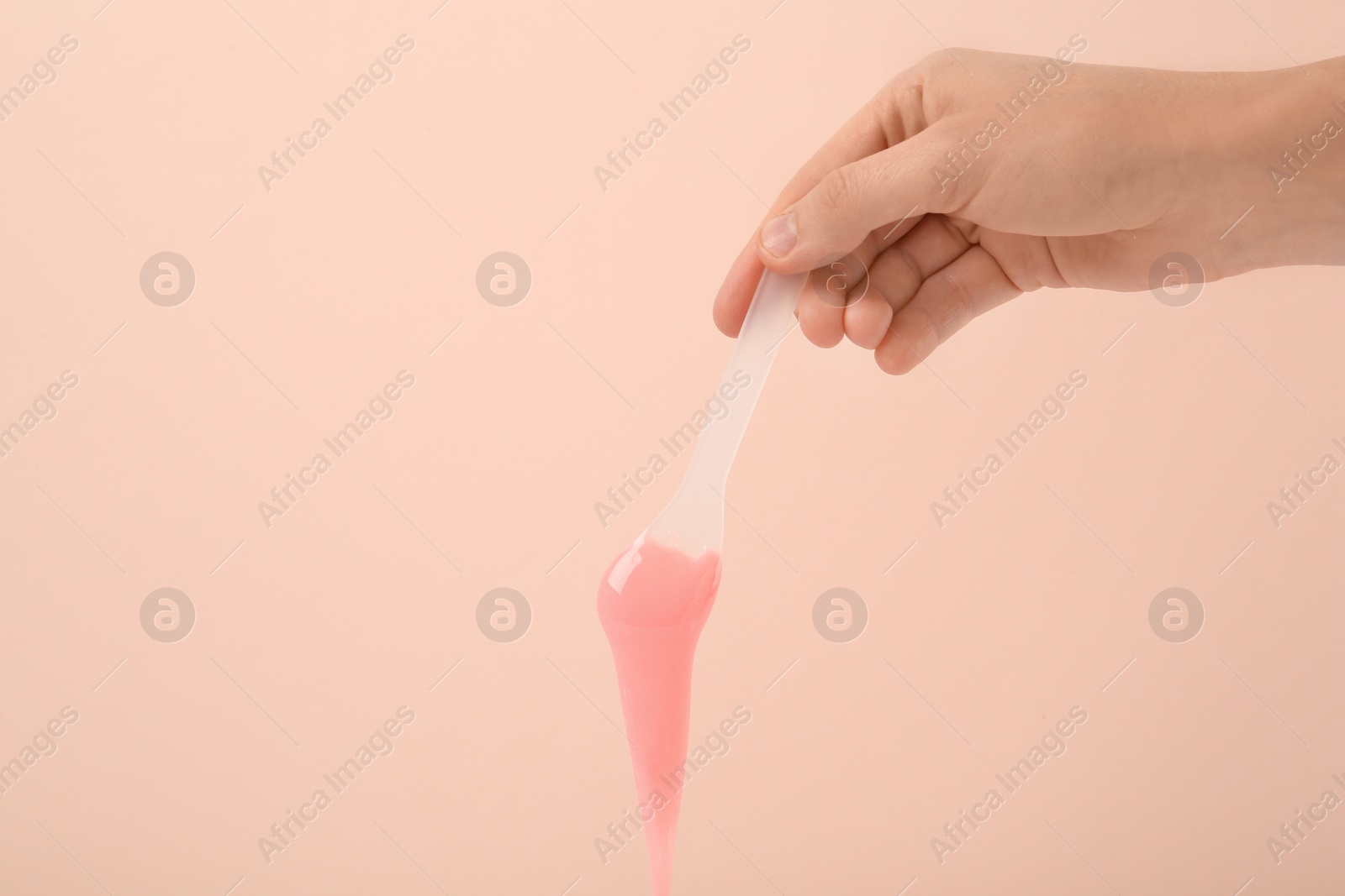 Photo of Woman holding spatula with hot depilatory wax on beige background, closeup. Space for text
