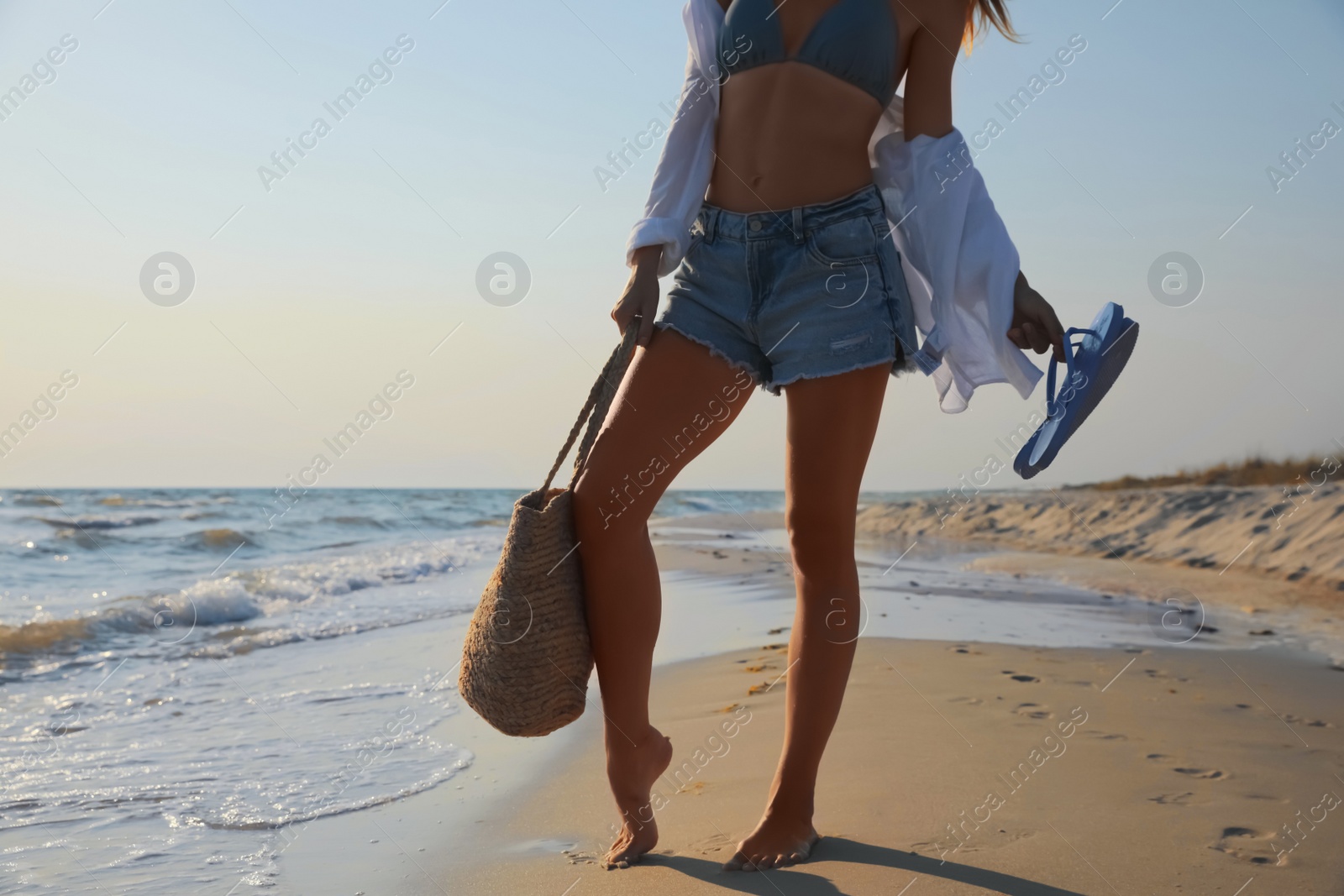 Woman with beach slippers and bag on sandy seashore, closeup Photo of Woman with beach slippers and bag on sandy seashore, closeup