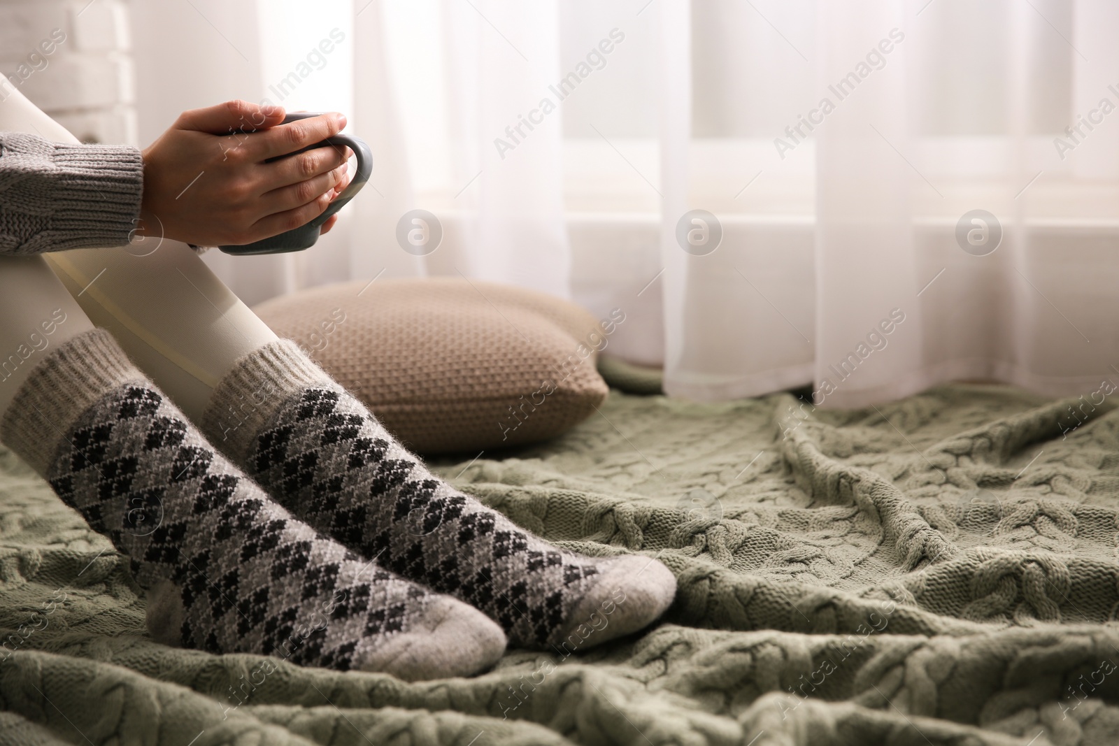 Woman relaxing with cup of hot winter drink on knitted plaid at home, closeup. Space for text Photo of Woman relaxing with cup of hot winter drink on knitted plaid at home, closeup. Space for text
