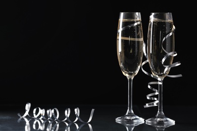 Glasses of champagne and serpentine streamers on black background. Space for text Photo of Glasses of champagne and serpentine streamers on black background. Space for text
