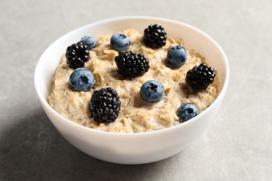 Tasty oatmeal porridge with blackberries and blueberries in bowl on grey table Photo of Tasty oatmeal porridge with blackberries and blueberries in bowl on grey table