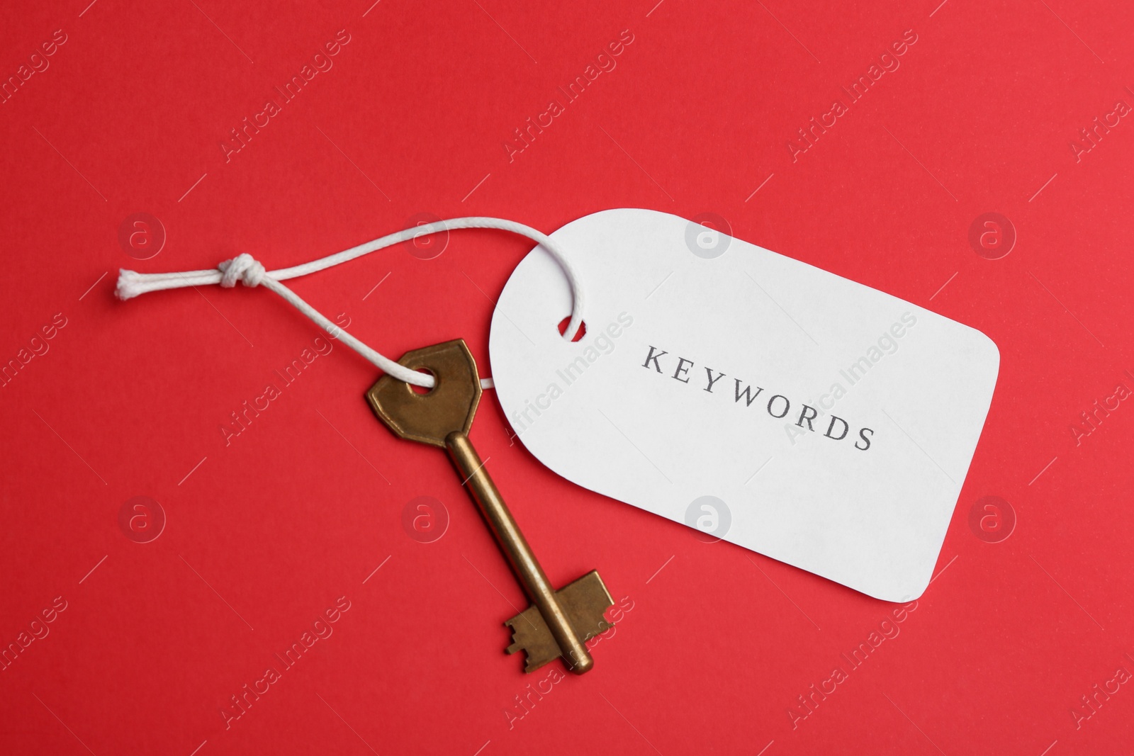 Metal key and tag wIth word KEYWORDS on red background, top view Photo of Metal key and tag wIth word KEYWORDS on red background, top view