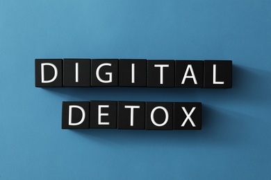 Black cubes with words DIGITAL DETOX on blue background, flat lay Photo of Black cubes with words DIGITAL DETOX on blue background, flat lay