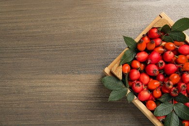Ripe rose hip berries with green leaves in crate on wooden table, top view. Space for text Photo of Ripe rose hip berries with green leaves in crate on wooden table, top view. Space for text